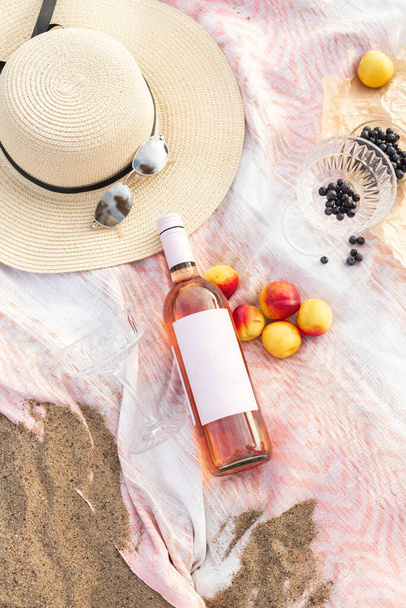 Letni piknik plażowy na wybrzeżu. Butelka różanego wina, owoce, letnie dodatki. Romantyczna koncepcja imprezy. Widok z góry - Zdjęcie, obraz