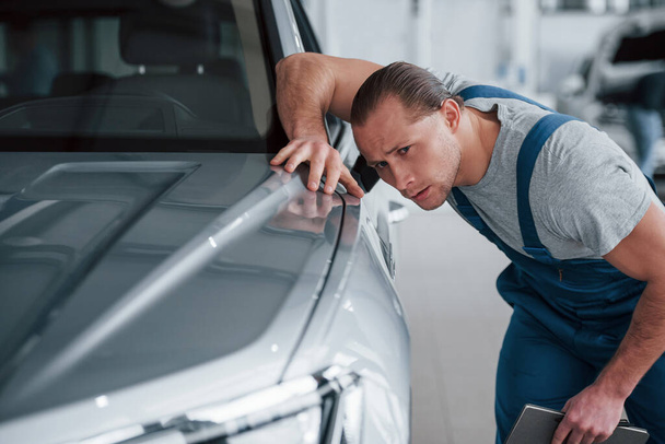After professional repairing. Man looking at perfectly polished silver colored car. - Foto, Imagen
