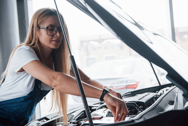 Replacement of a parts. On the lovely job. Car addicted woman repairs black automobile indoors. - Foto, imagen