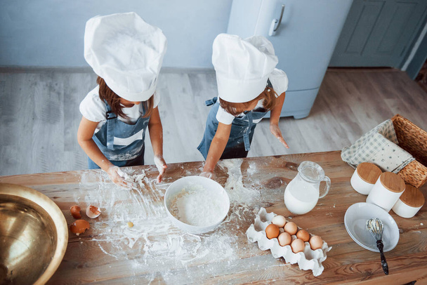 Horní pohled. Rodinné děti v bílé kuchařské uniformě připravují jídlo v kuchyni. - Fotografie, Obrázek