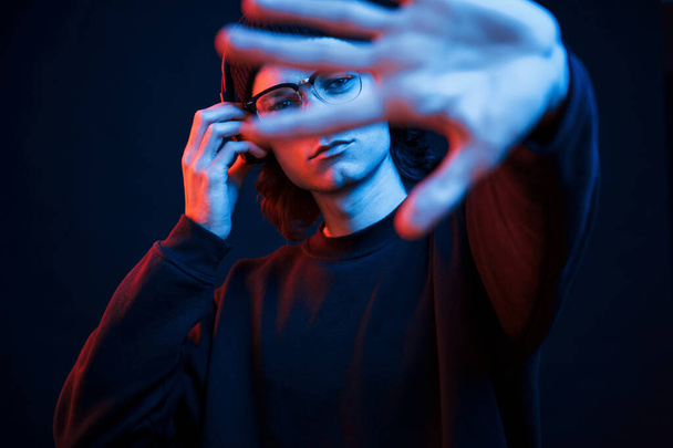 Left hand is blurred. Studio shot in dark studio with neon light. Portrait of serious man. - Photo, image
