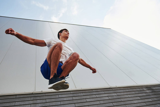 Into the air. Young sports man doing parkour in the city at sunny daytime. - Valokuva, kuva