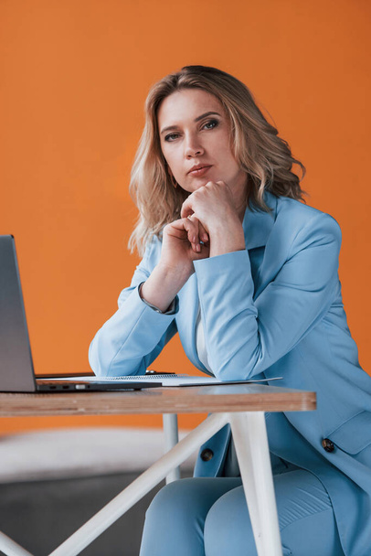 She listens to you carefully. Businesswoman with curly blonde hair indoors in room with orange colored wall and wooden table. - Фото, изображение