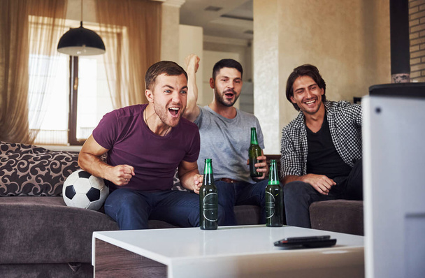 Excited three friends watching soccer on TV at home together. - Foto, Imagen