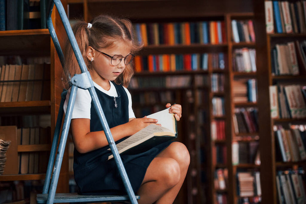School girl on the ladder in library full of books. Education conception. - Zdjęcie, obraz