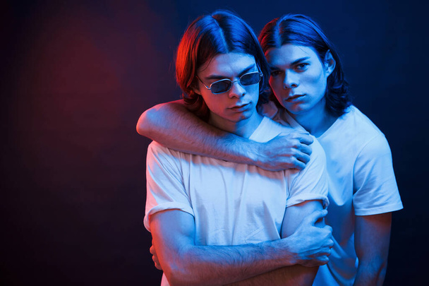 We must be together if we wanna be strong. Portrait of twin brothers. Studio shot in dark studio with neon light. - Zdjęcie, obraz