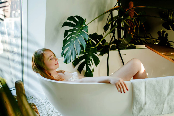 νεαρή ξανθιά γυναίκα ξαπλωμένη σε μια μπανιέρα. Η γυναίκα ξεκουράζεται στο μπάνιο.. - Φωτογραφία, εικόνα