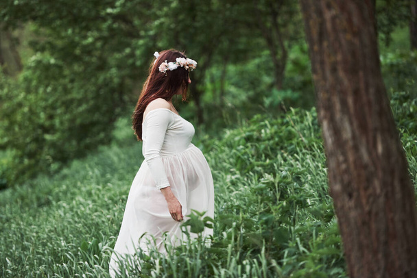 In the forest. Beautiful pregnant woman in dress have a walk outdoors. Positive brunette. - Foto, immagini