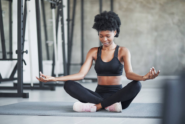 Practicing yoga. African american woman with curly hair and in sportive clothes have fitness day in the gym. - Foto, Imagem