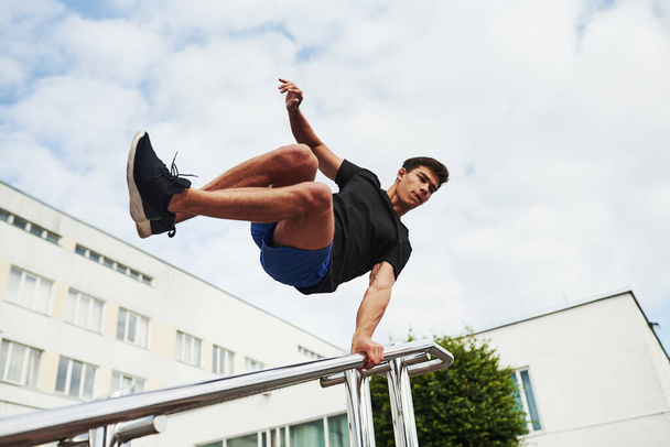Silver colored railings. Young sports man doing parkour in the city at sunny daytime. - Foto, afbeelding
