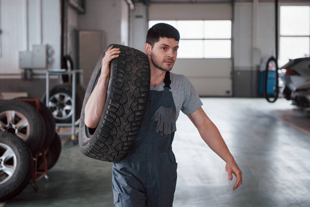 Another one wheel. Mechanic holding a tire at the repair garage. Replacement of winter and summer tires. - Photo, image