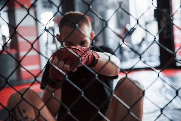 From down position. Young boxer in red bandages have exercise. In the gym on the cage. - Fotografie, Obrázek