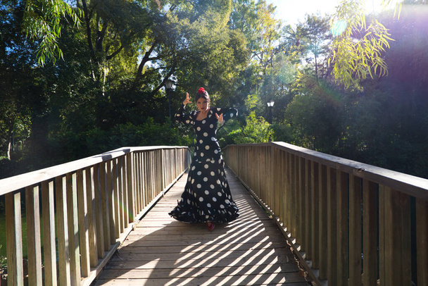 gyönyörű spanyol barna flamenco táncos nő egy tipikus flamenco jelmez fehér polka pöttyök táncolnak egy fa kifutón az utcán. Az emberiség flamenco kulturális öröksége. - Fotó, kép