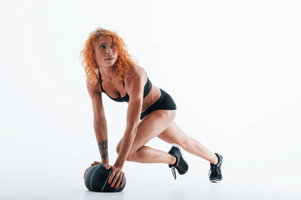 Posing for a camera with soccer ball. Particle view. Redhead female bodybuilder is in the studio on white background. - Foto, Imagen