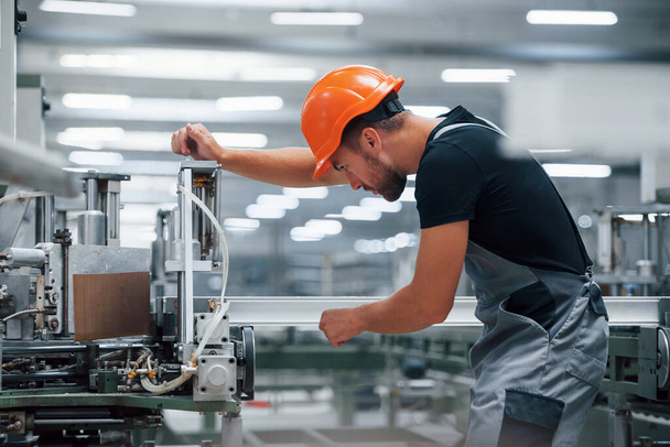 Operator of machine. Industrial worker indoors in factory. Young technician with orange hard hat. - Fotó, kép