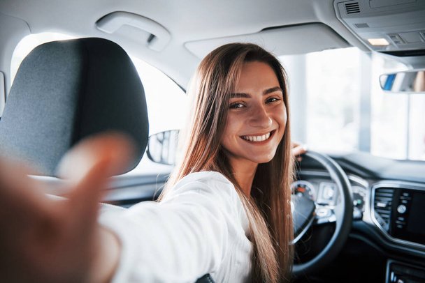 Making selfie. Cheerful female driver is in her new car. Interior of modern automobile. - Fotó, kép