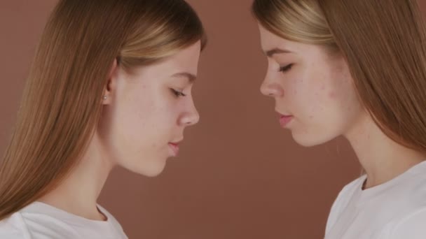 Портрет с крупным планом молодых сестер-близнецов, касающихся лбов на коричневом фоне - Кадры, видео