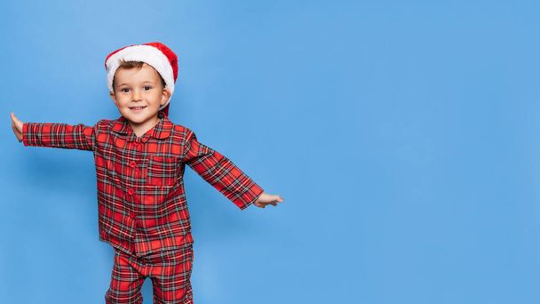 Studyjne ujęcie szczęśliwego chłopca w świątecznej piżamie, zabawiającego się i uśmiechającego. Miejsce na twoją wiadomość. Pojęcie wakacji. - Zdjęcie, obraz