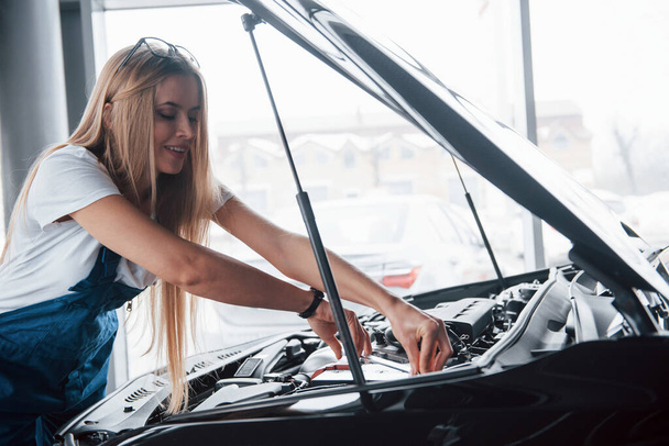 Under the hood. On the lovely job. Car addicted woman repairs black automobile indoors. - Fotoğraf, Görsel