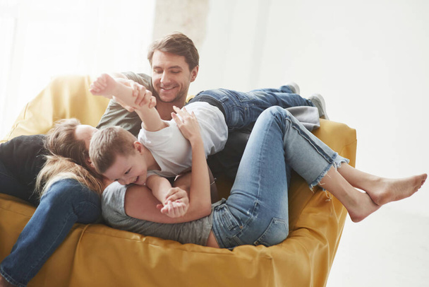 A giocare. Buona famiglia si divertono sul divano giallo nel soggiorno della loro nuova casa. - Foto, immagini