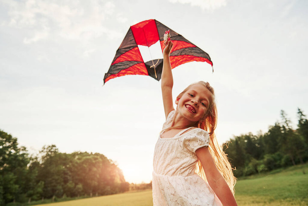 Watch at my kite, it's flying. Happy girl in white clothes have fun in the field. Beautiful nature. - Valokuva, kuva