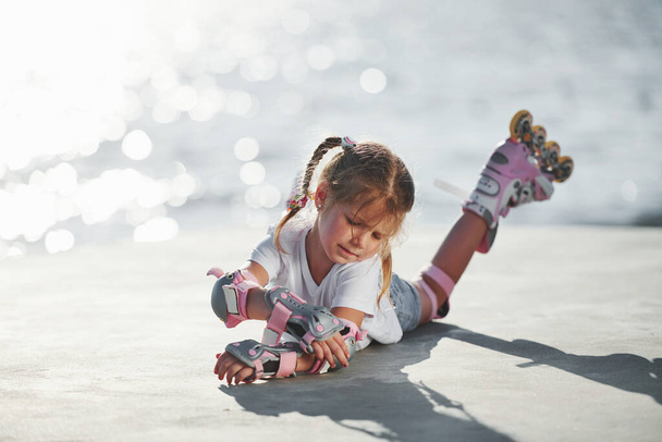 Lying down. Cute little girl with roller skates outdoors near the lake at background. - 写真・画像