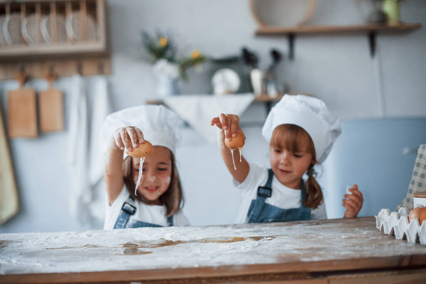 Playing with eggs. Family kids in white chef uniform preparing food on the kitchen. - Valokuva, kuva