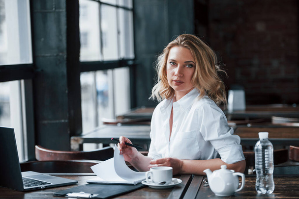Turning the page. Businesswoman with curly blonde hair indoors in cafe at daytime. - Foto, afbeelding
