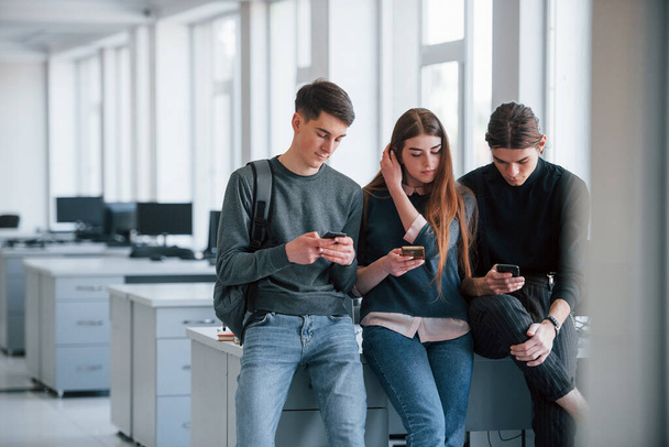 Internet addiction. Group of young people in casual clothes have a rest in the modern office. - Foto, afbeelding