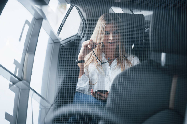 Unusual interesting angle. Smart businesswoman sits at backseat of the luxury car with black interior. - Zdjęcie, obraz