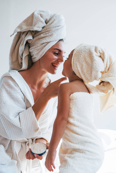 Using cream to clear skin. Young mother with her daugher have beauty day indoors in white room. - Foto, afbeelding