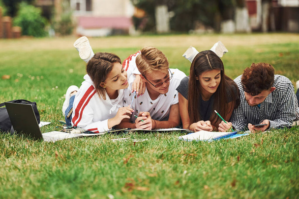 Writing on paper. front view. Group of young students in casual clothes on green grass at daytime. - Foto, Bild