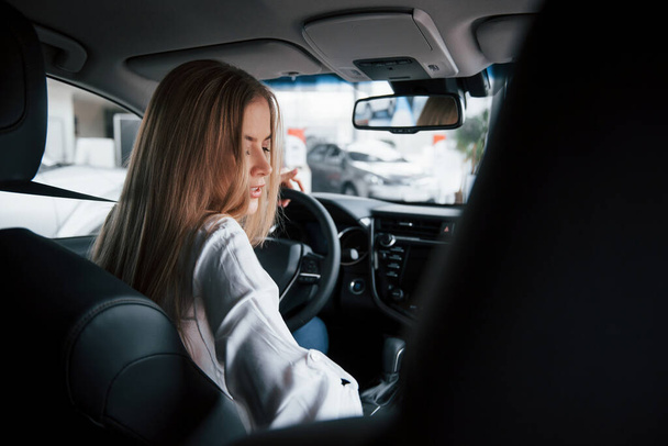 Rear view. Beautiful blonde girl sitting in the new car with modern black interior. - Fotó, kép