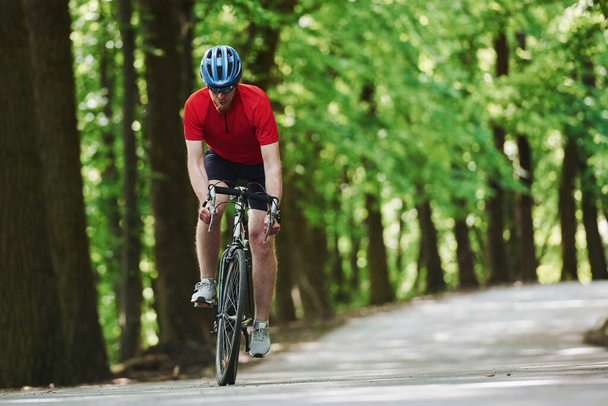Leisure activities. Cyclist on a bike is on the asphalt road in the forest at sunny day. - Photo, image