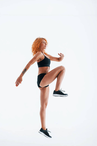 Having exercise. Redhead female bodybuilder is in the studio on white background. - Фото, изображение