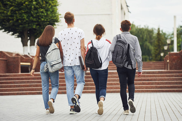 Visão traseira. Grupo de jovens estudantes em roupas casuais perto da universidade durante o dia. - Foto, Imagem