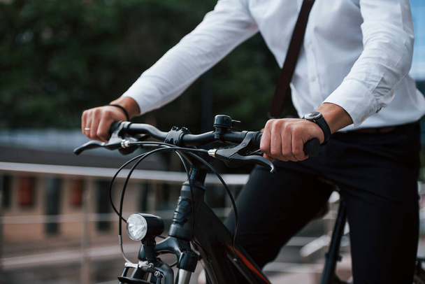 Close up view. Businessman in formal clothes with black bicycle is in the city. - Foto, afbeelding