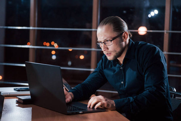 Nervous guy. Stylish businessman in eyewear works alone in the office at nightime. - Photo, image