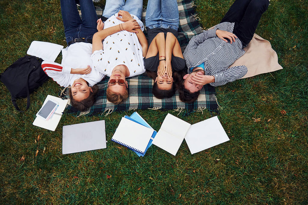 Having good rest. Group of young students in casual clothes on green grass at daytime. - Photo, image