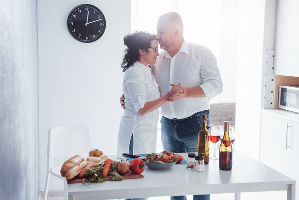 Hearts burst into fire. Senior man and his wife in white shirt have romantic dinner on the kitchen. - Foto, Bild