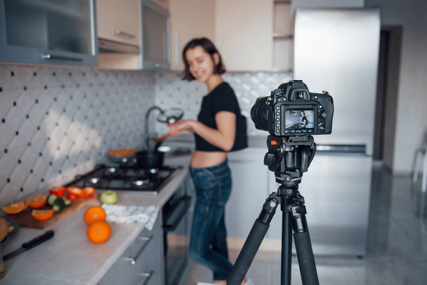 Focus on the camera. Girl in the modern kitchen at home at her weekend time in the morning. - Foto, afbeelding