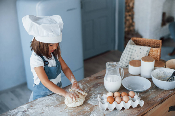 Cute kid in white chef uniform preparing food on the kitchen. - Photo, Image