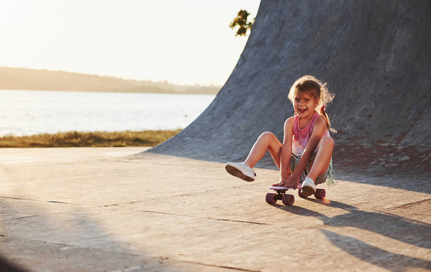 Sits on the skate. Sunny day. Kid have fun at the ramp. Cheerful little girl. - Fotoğraf, Görsel