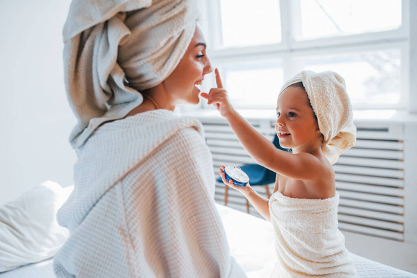 Using cream to clear skin. Young mother with her daugher have beauty day indoors in white room. - Foto, Imagen