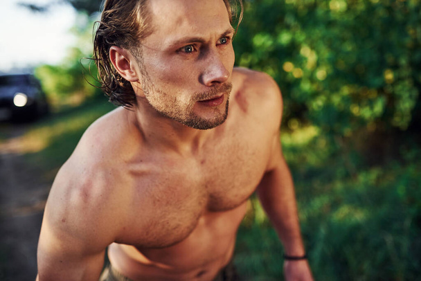 Close up portrait. Handsome shirtless man with muscular body type is in the forest at daytime. - Фото, зображення