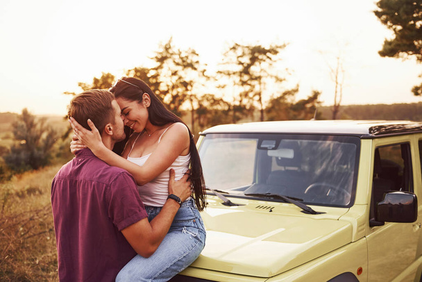 Lovely couple kissing outdoors. Girl sits on green jeep. Beautiful sunny evening. - Foto, Bild