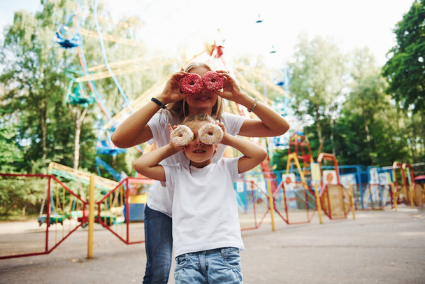 Having fun with donuts. Cheerful little girl her mother have a good time in the park together near attractions. - Foto, imagen