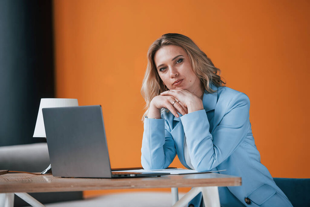 What kind of financial problem do you have. Businesswoman with curly blonde hair indoors in room with orange colored wall and wooden table. - Foto, imagen