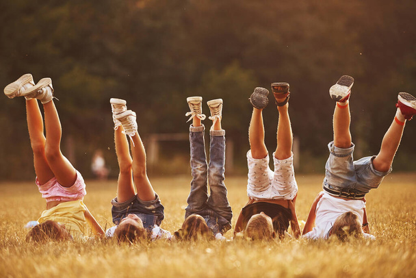 Kids resting in the field at sunny daytime together. Raising legs up. - Foto, afbeelding
