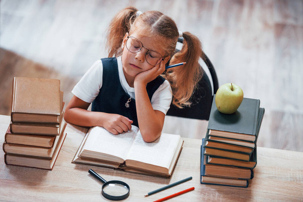 Feels bored and tired. Cute little girl with pigtails is in the library. Apple on the books. - Fotoğraf, Görsel
